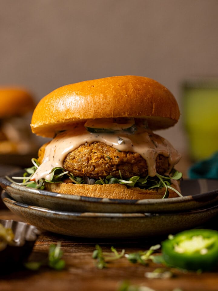 Up close shot of veggie burger on two plates with a drink in background.