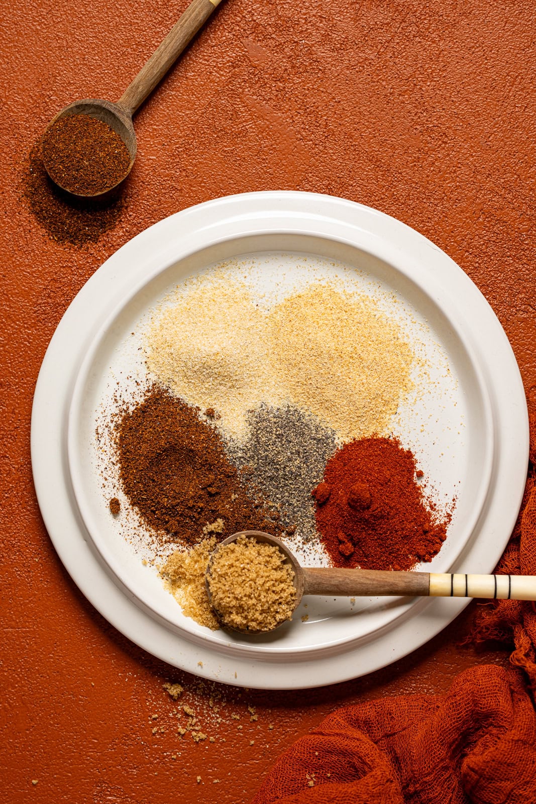 All seasonings grouped together on a white plate with two wooden spoons.