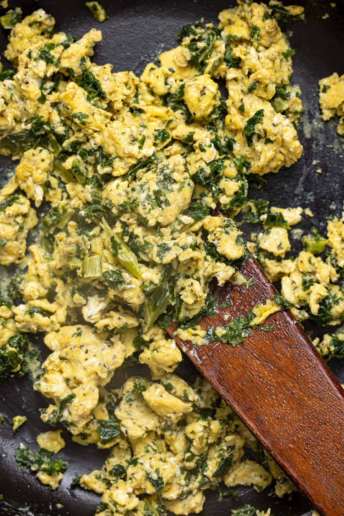 Scrambled eggs in a skillet with a wooden spoon.