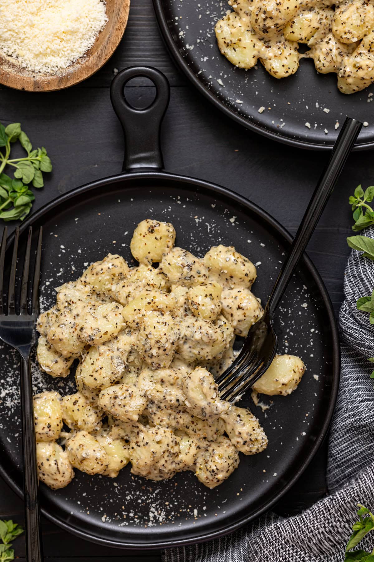 Two plates of gnocchi on a black wood table with two forks.