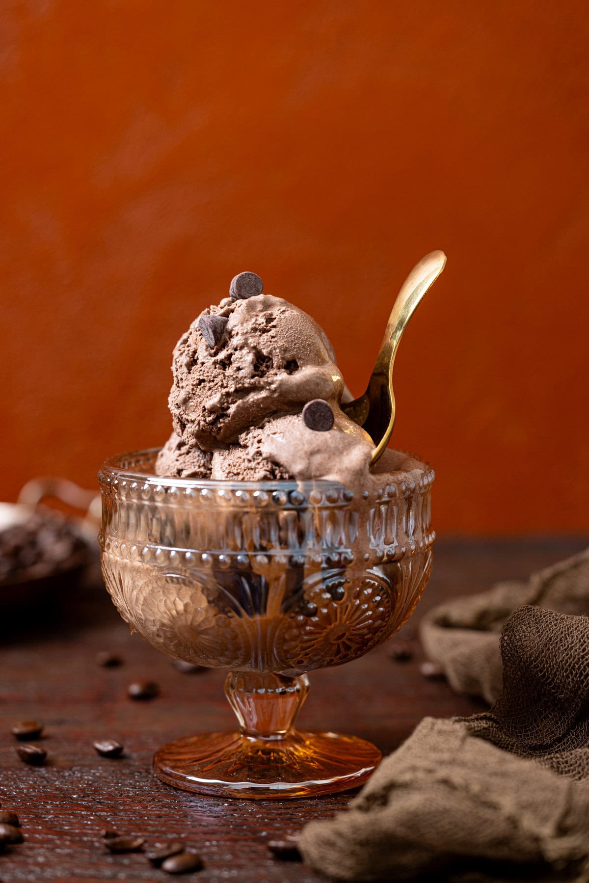 Shot of chocolate ice cream in a bowl with a gold spoon with a burnt orange background. 