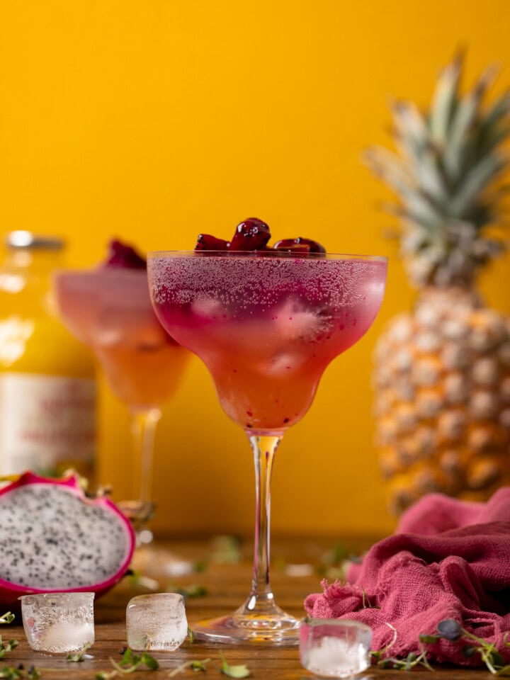 Two glasses of mocktail with pineapple and dragonfruit in the background.