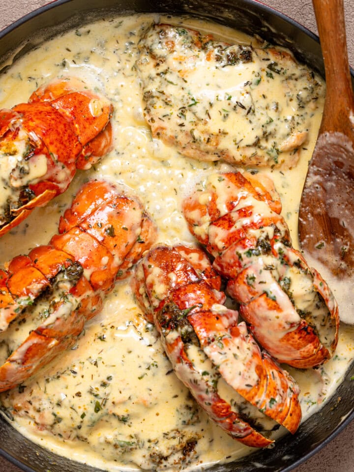 Up close shot of lobster tails and salmon in creamy sauce in a red skillet with a spoon.