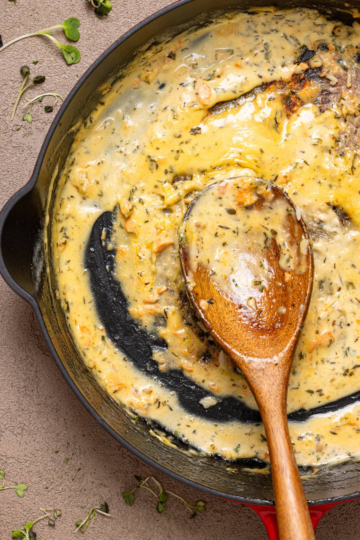 Red skillet with creamy sauce and a spoon fully eaten.