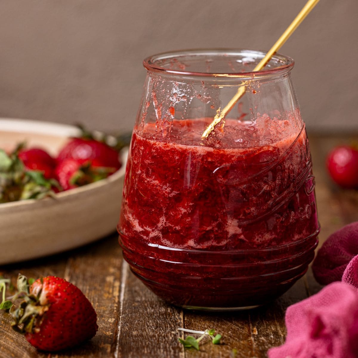 Strawberry jam in a jar with a spoon and strawberries.