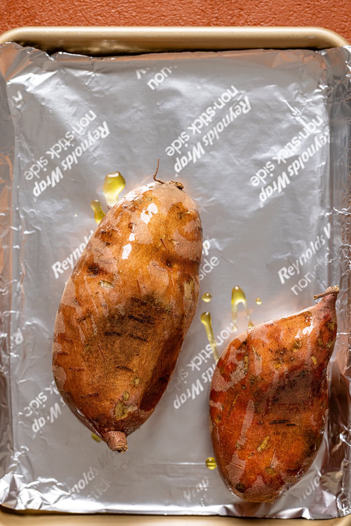 Prepped sweet potatoes with olive oil on a baking sheet with foil paper.