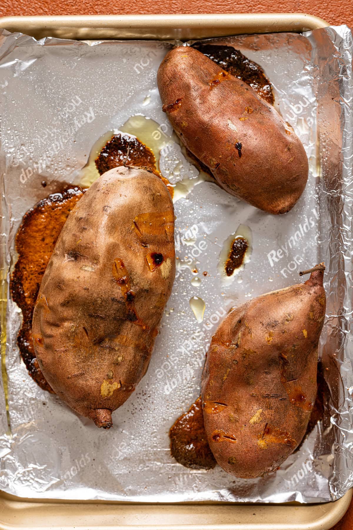 Baked sweet potatoes on a baking sheet with foil paper.