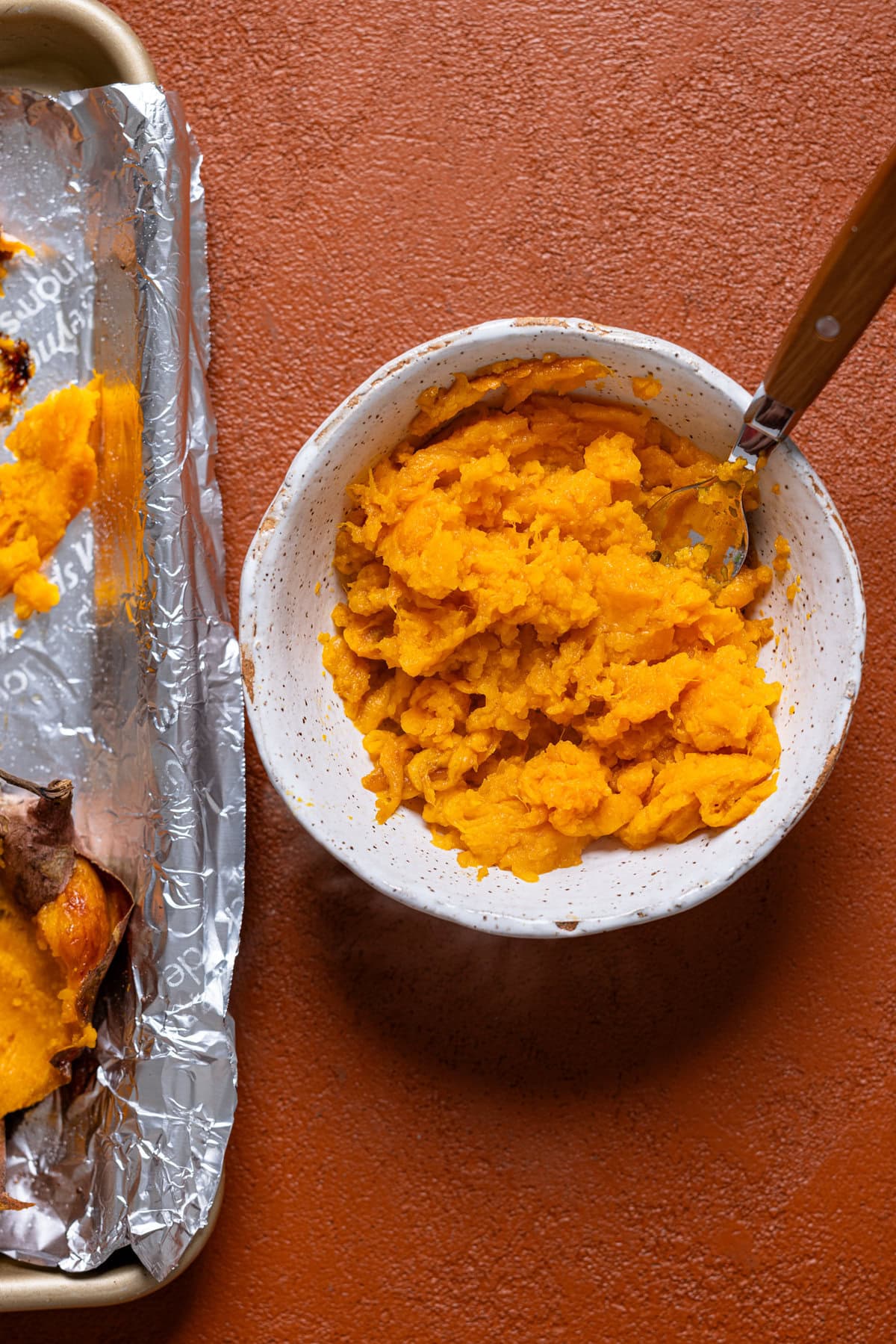 Scooped flesh of baked sweet potatoes in a white bowl with a spoon.