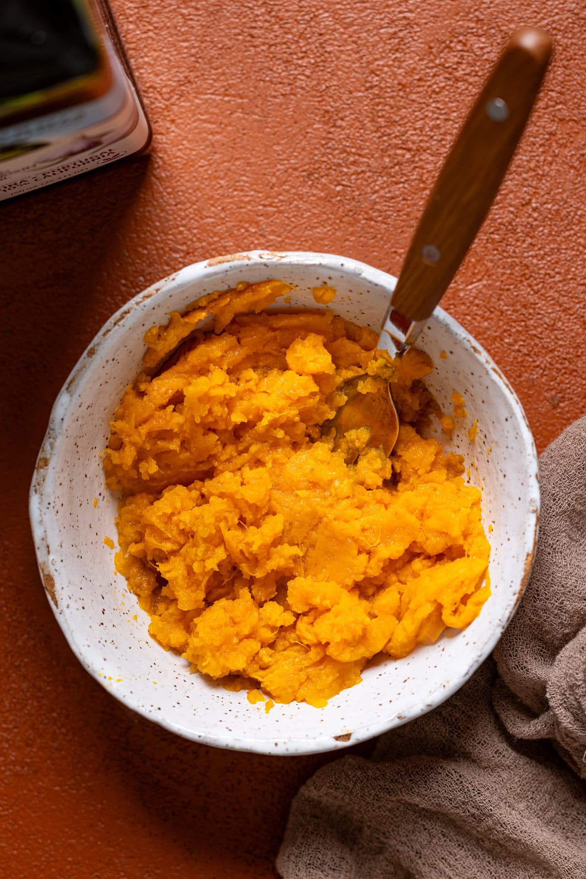 Smashed sweet potato in a white bowl with a spoon.