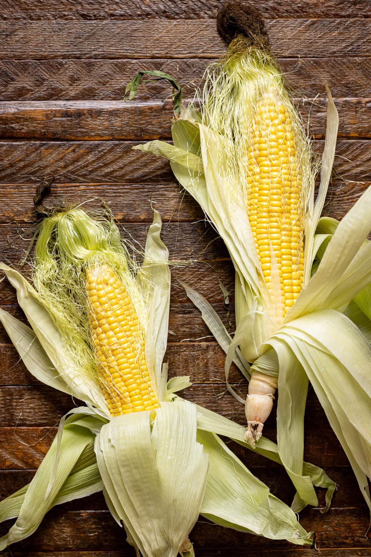 Ear of corn with open husks on a brown wood table.