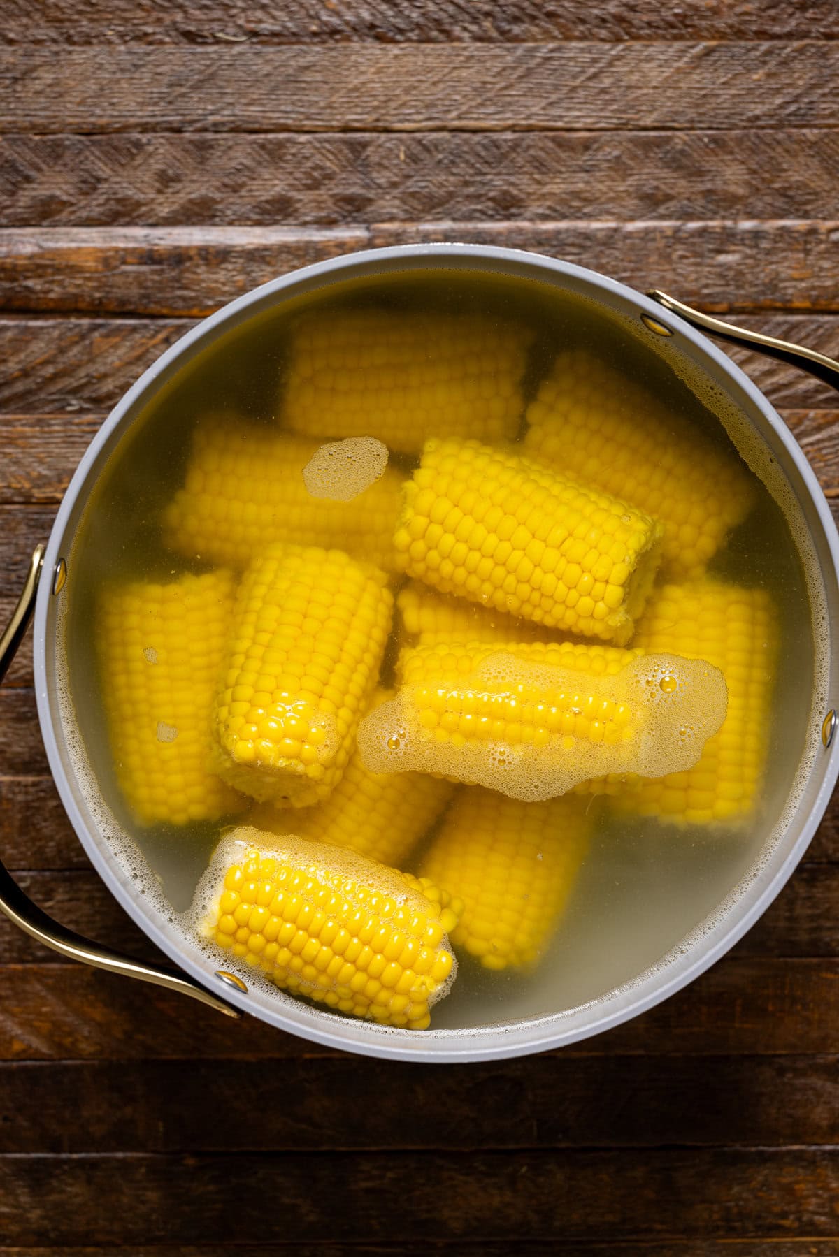 Boiled corn in a large pot of water on a brown wood table.