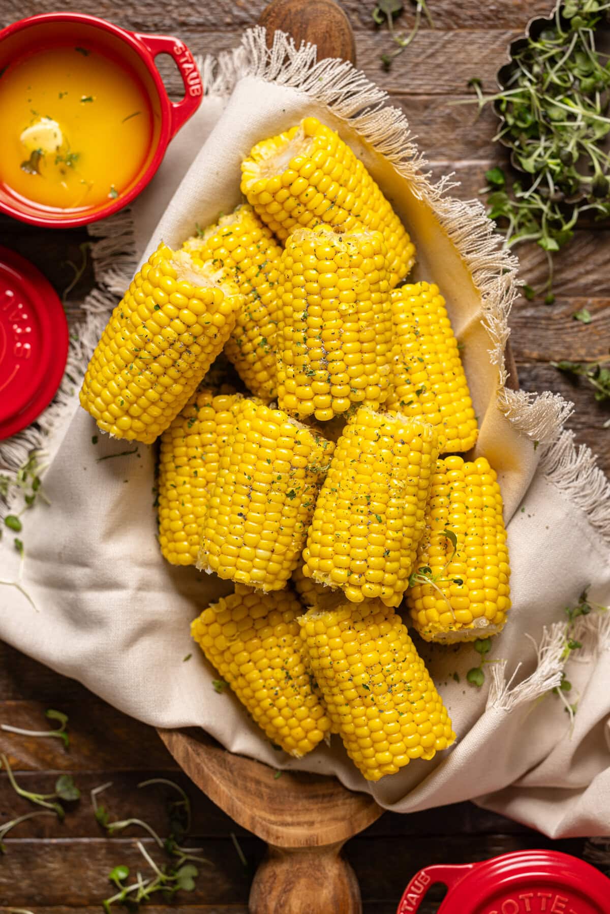 Corn in a wooden serving platter with melted butter and garnish.