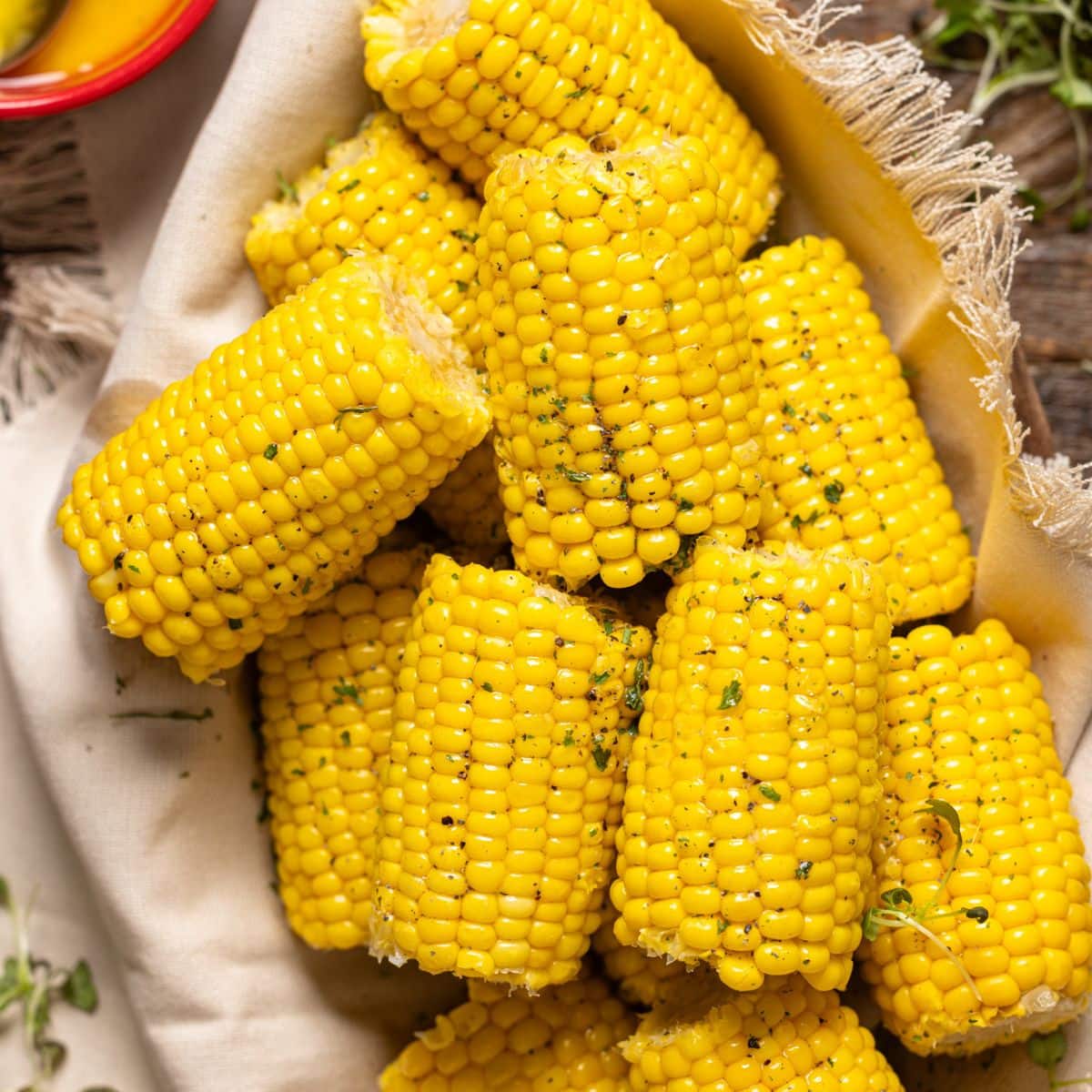 Corn on a wooden platter with melted butter and a spoon and red mini pots.