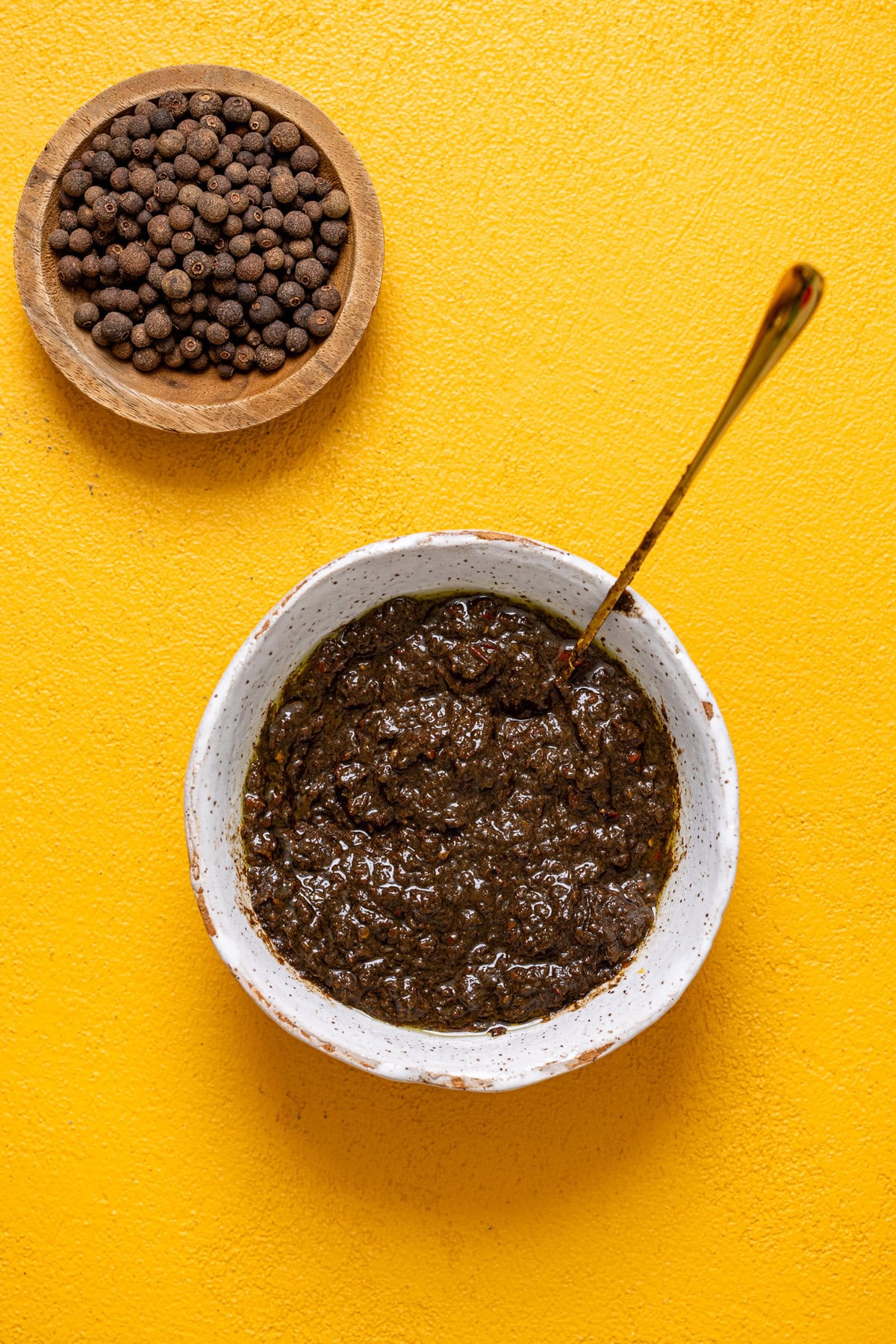 Jerk marinade in a white bowl with a spoon on a yellow table.