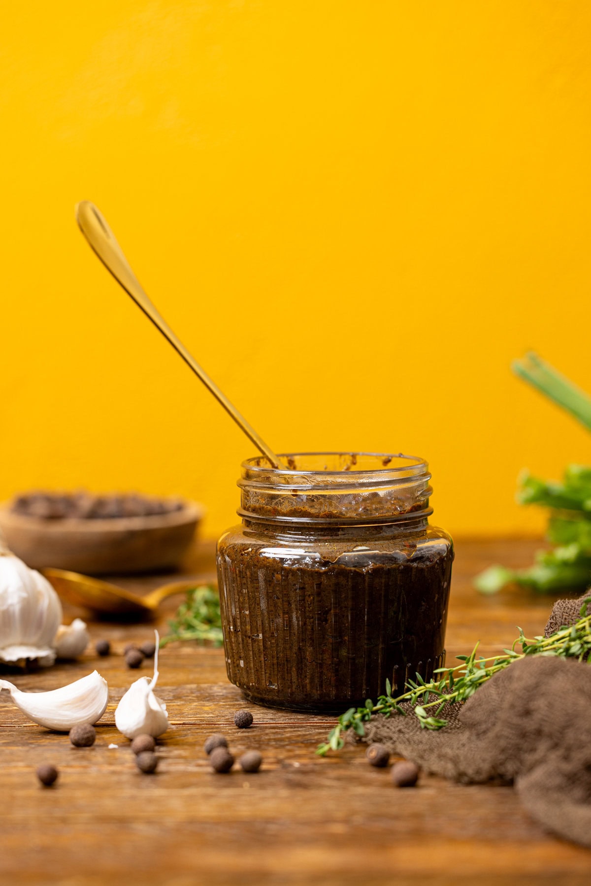 Jerk marinade in a jar on a brown wood table with a yellow background. 