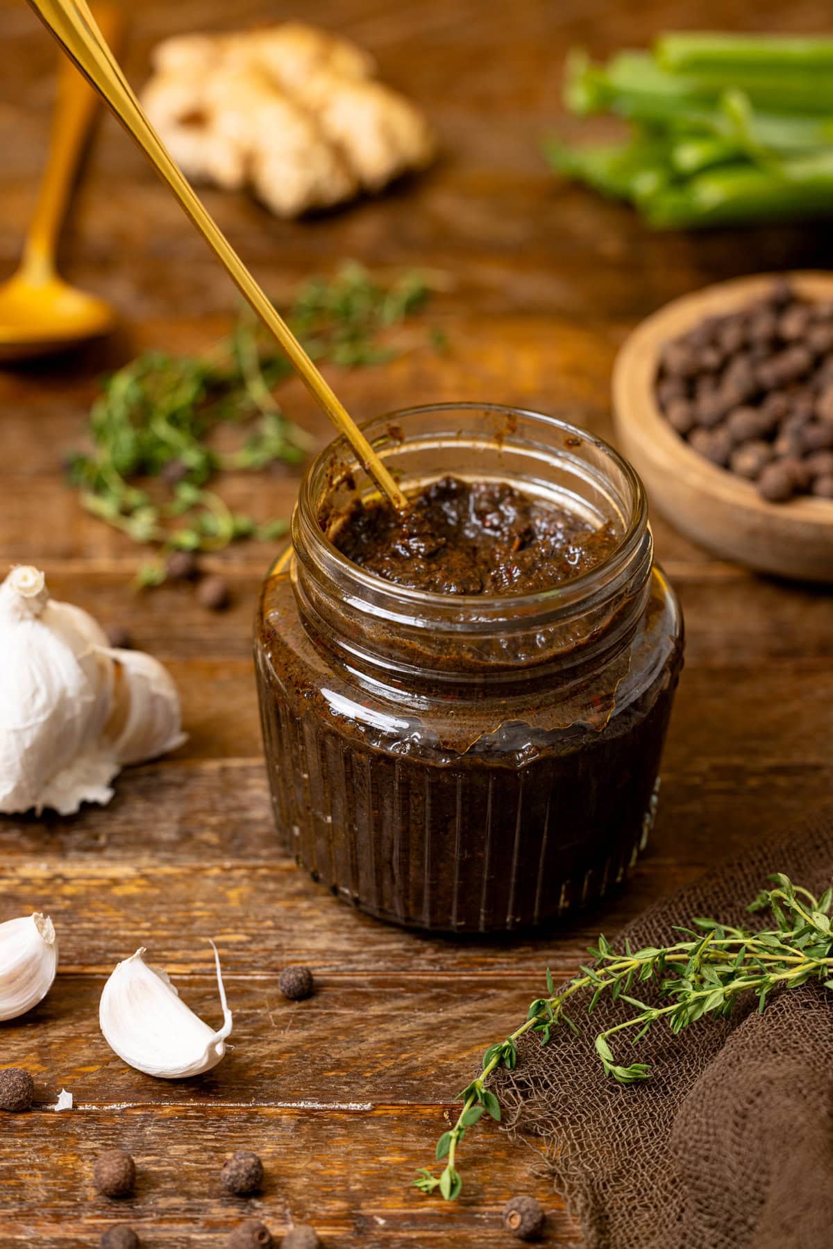 Jerk marinade on a brown wood table with garlic, thyme, and ingredients. 