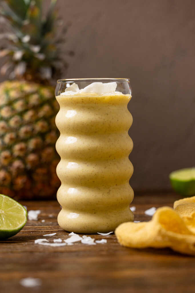 A glass of smoothie with a pineapple and lime.