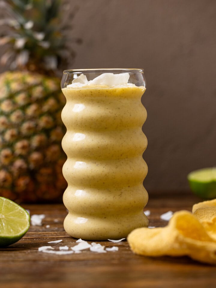A glass of smoothie with a pineapple and lime.