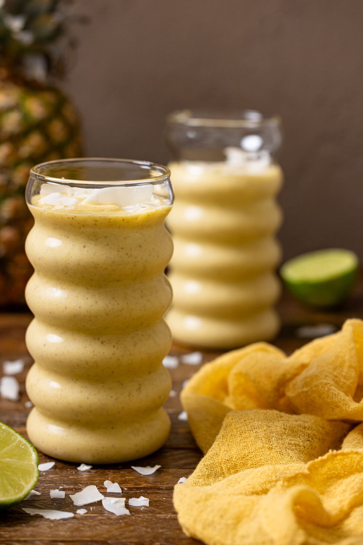 Two glasses of mango smoothies on a brown wood table with a pineapple. 