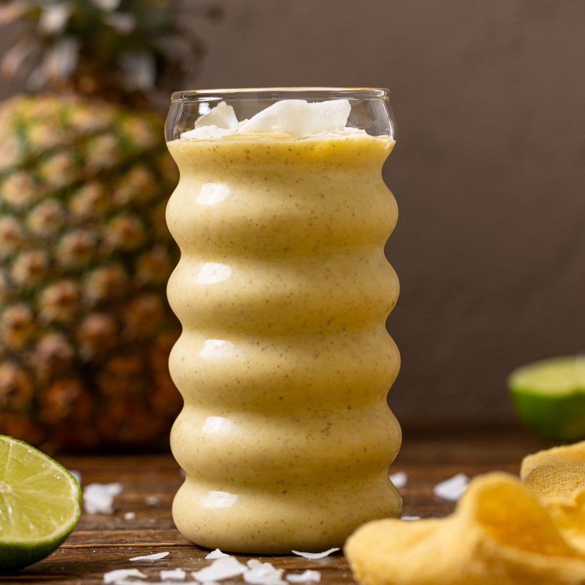 A glass of smoothie with a pineapple and lime.