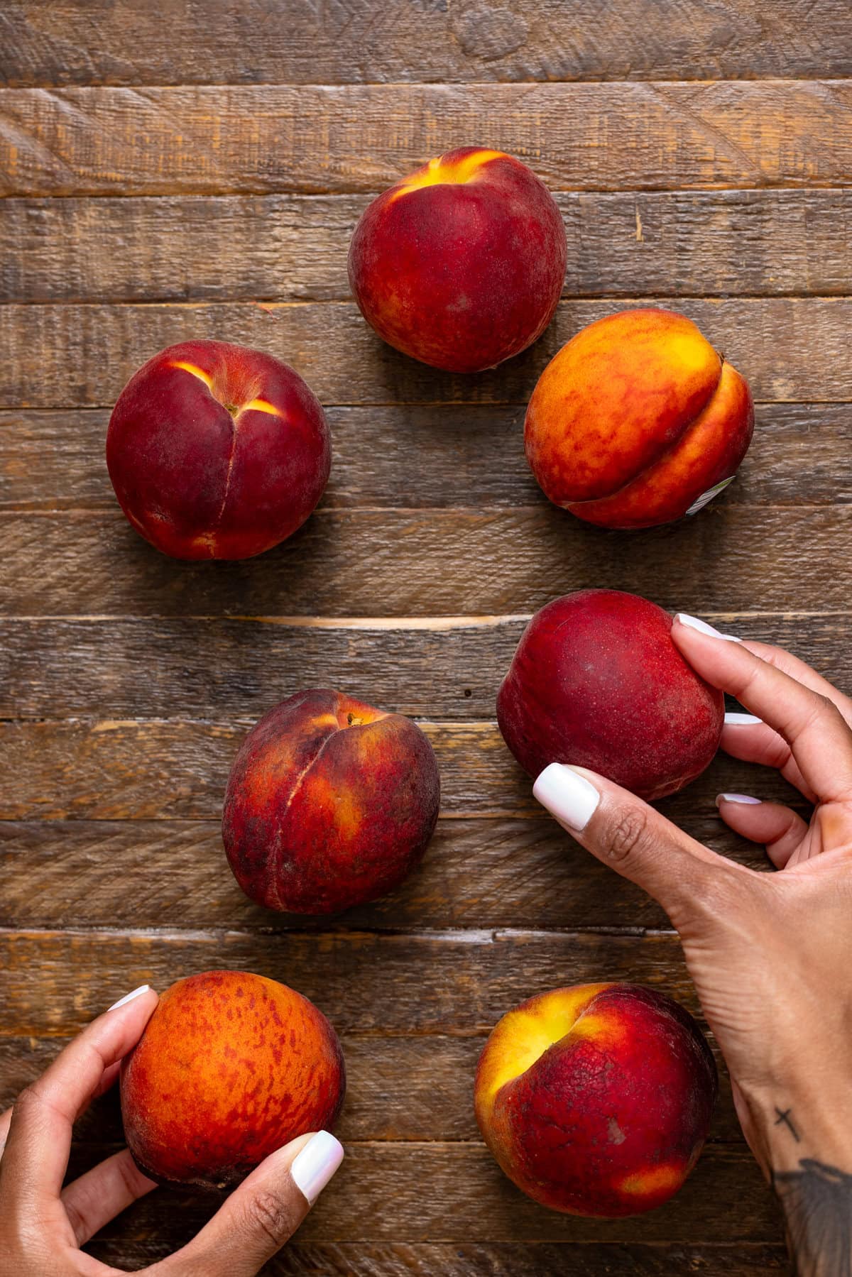 Fresh peaches on a brown wood table being held with hands.