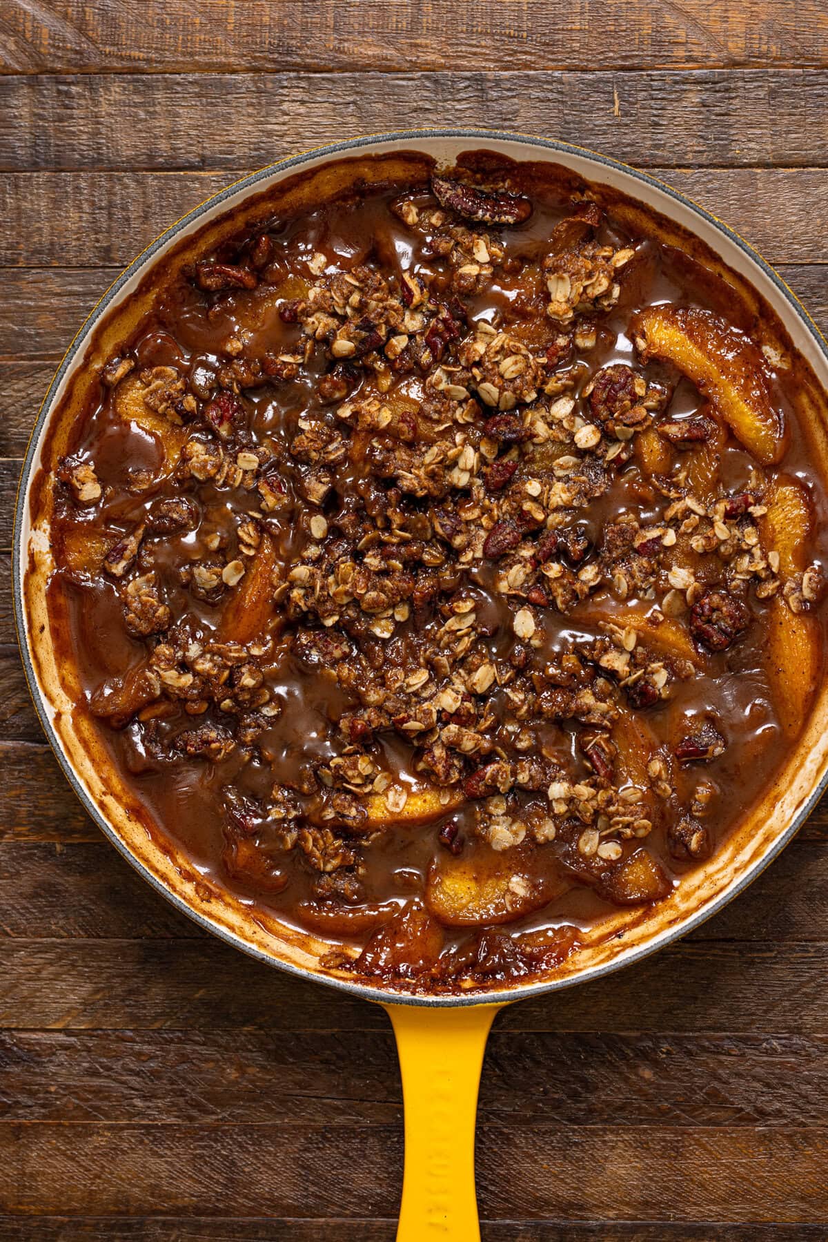 Baked peach crisp in a skillet on a brown wood table.