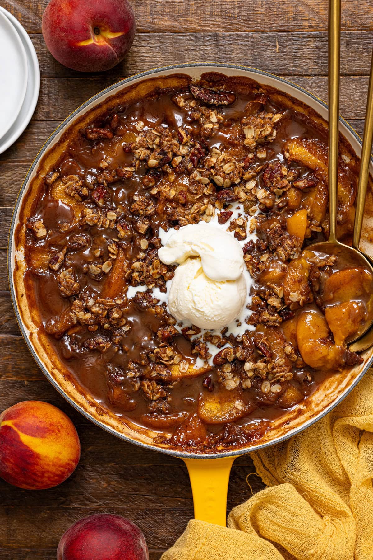 Baked peach crisp in a skillet with two spoon and a scoop of ice cream.