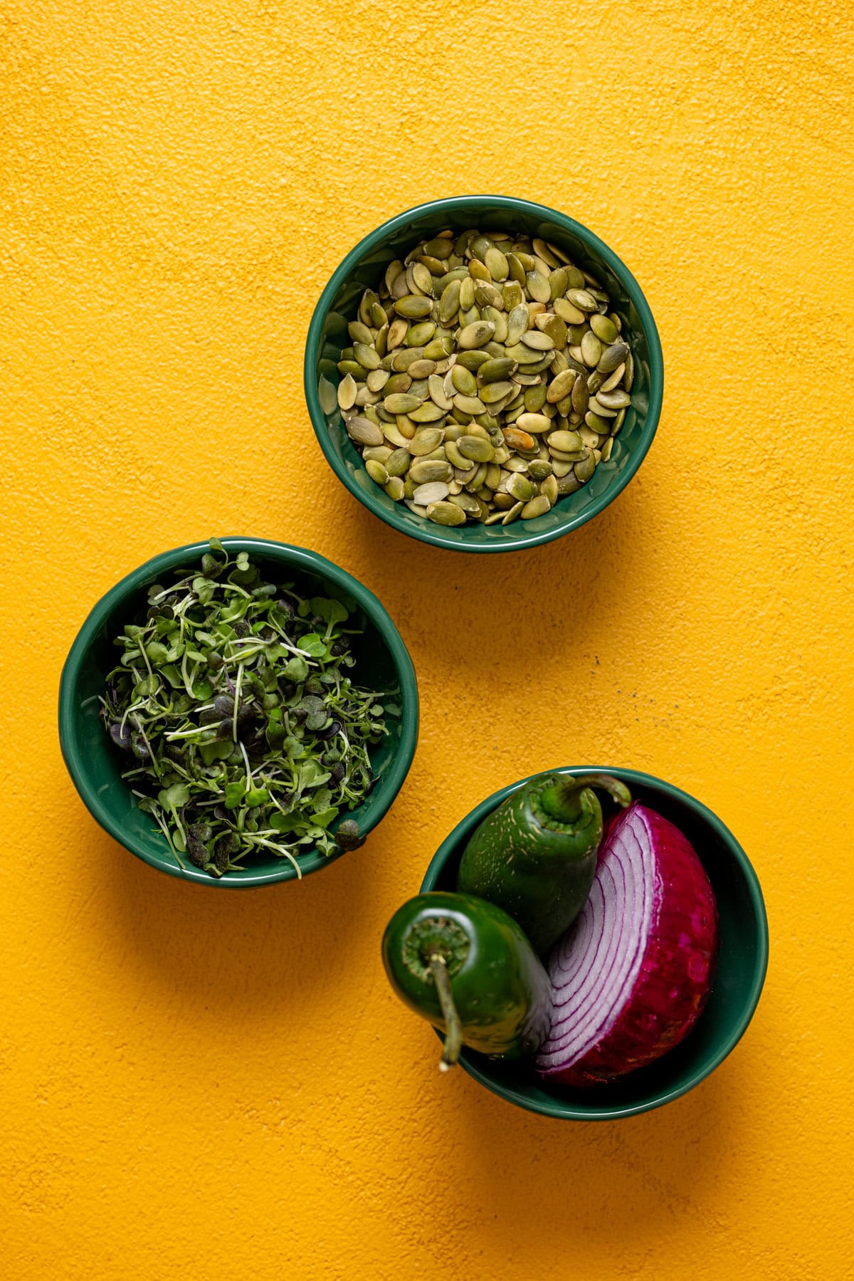 Ingredients in green bowls on a yellow table.