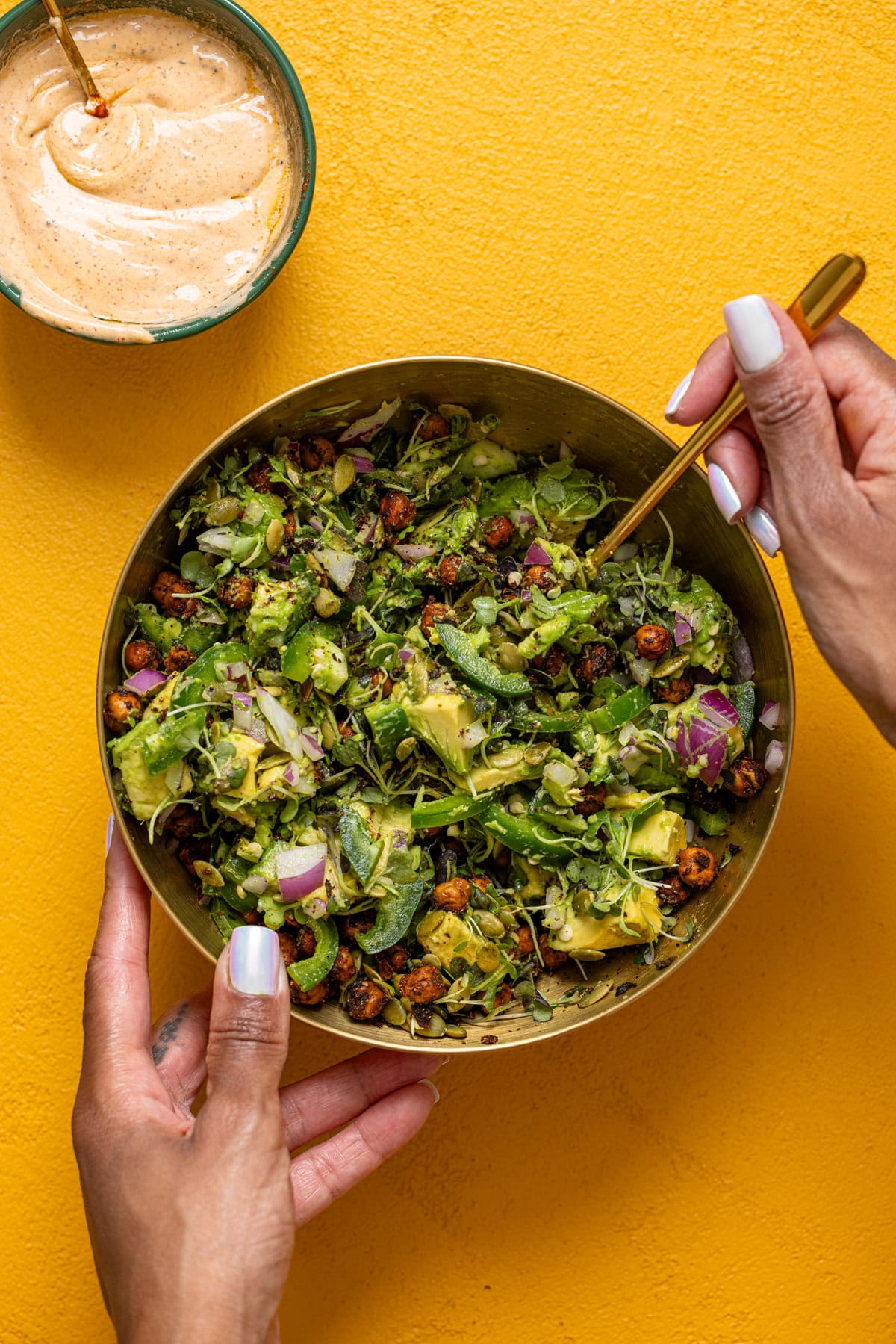 Salad ingredients in a gold bowl being stirred together with a spoon.