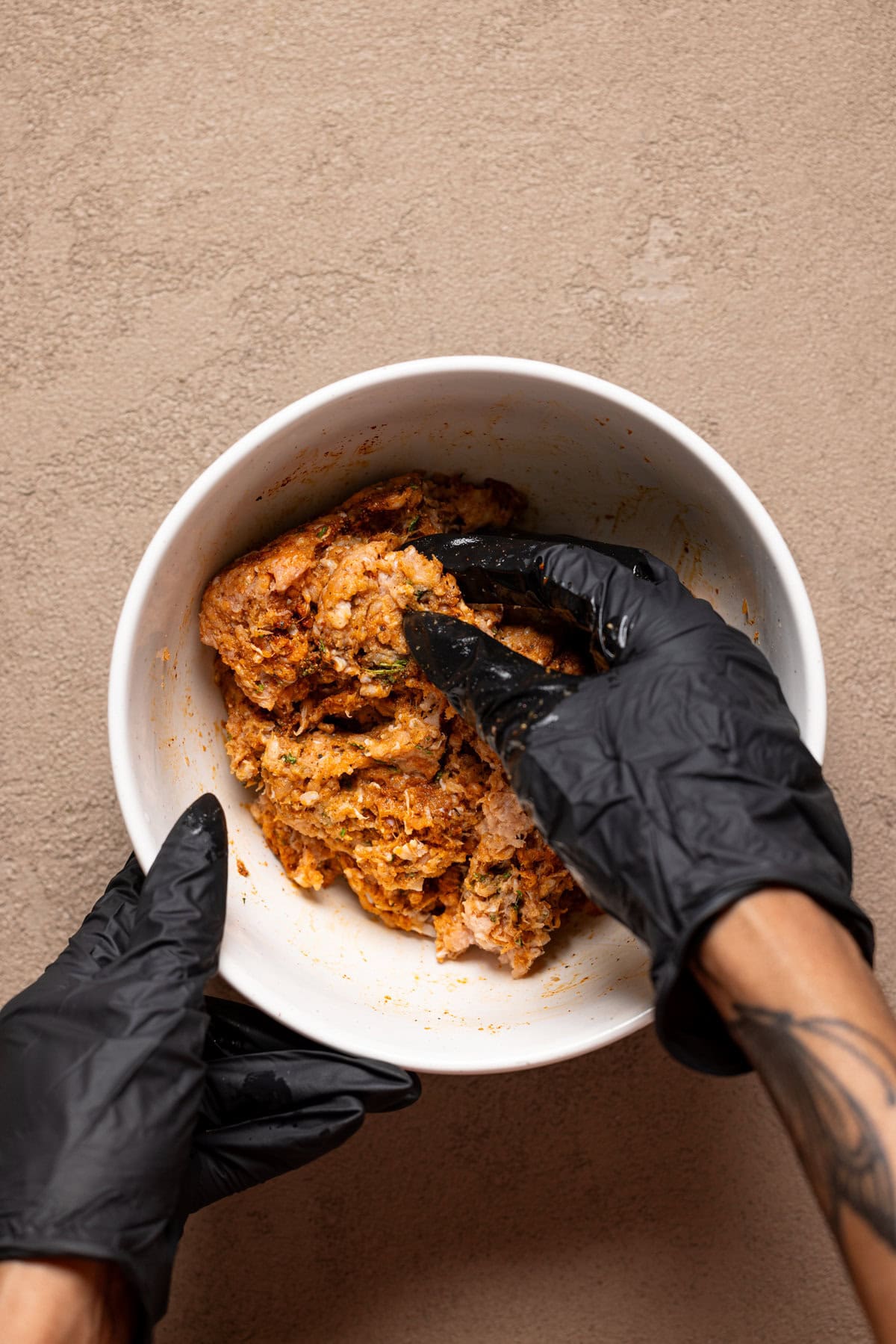 Turkey meat being stirred together with hands in black gloves.