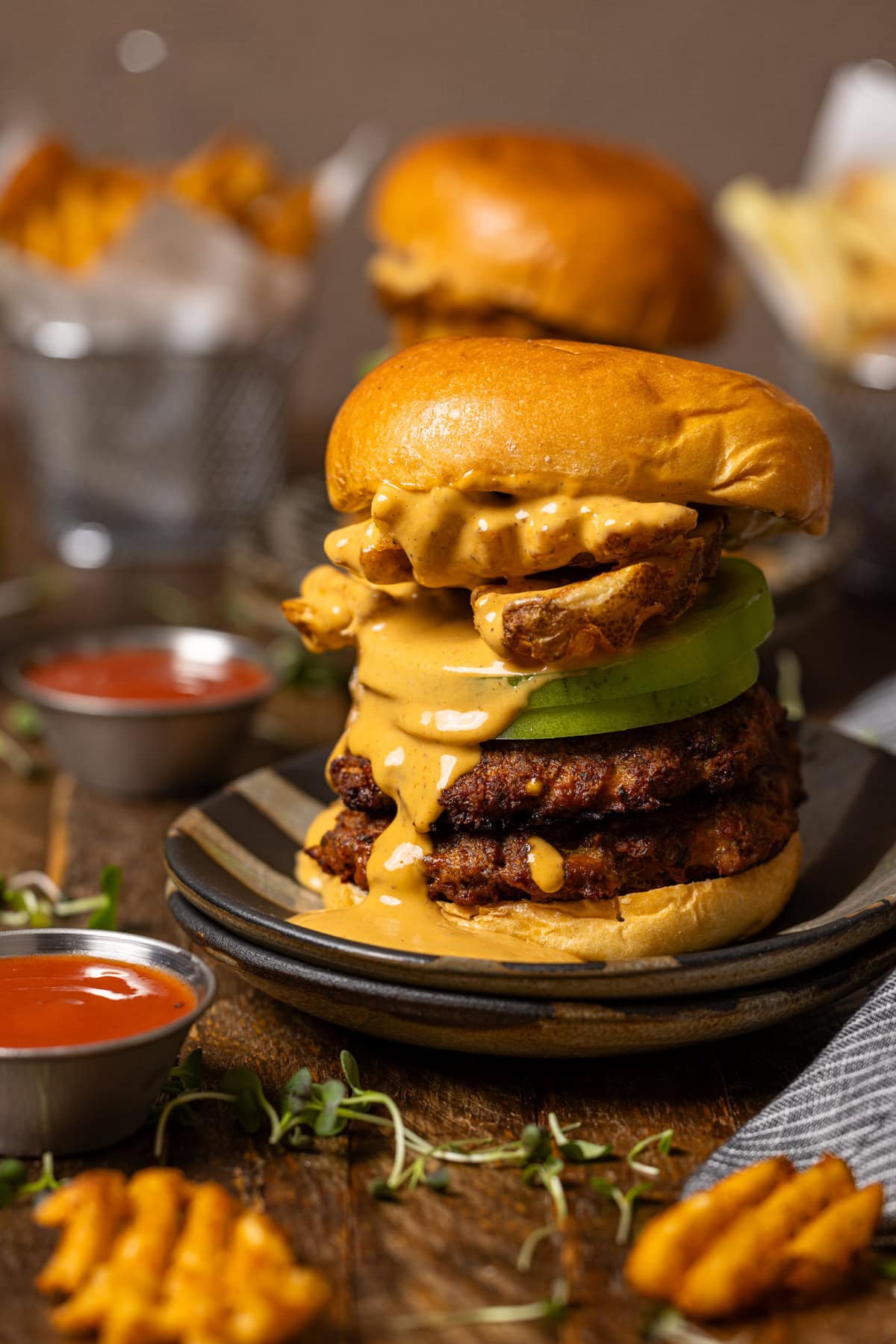 Smash burger on stacked plates with sauces and fries on the side. 