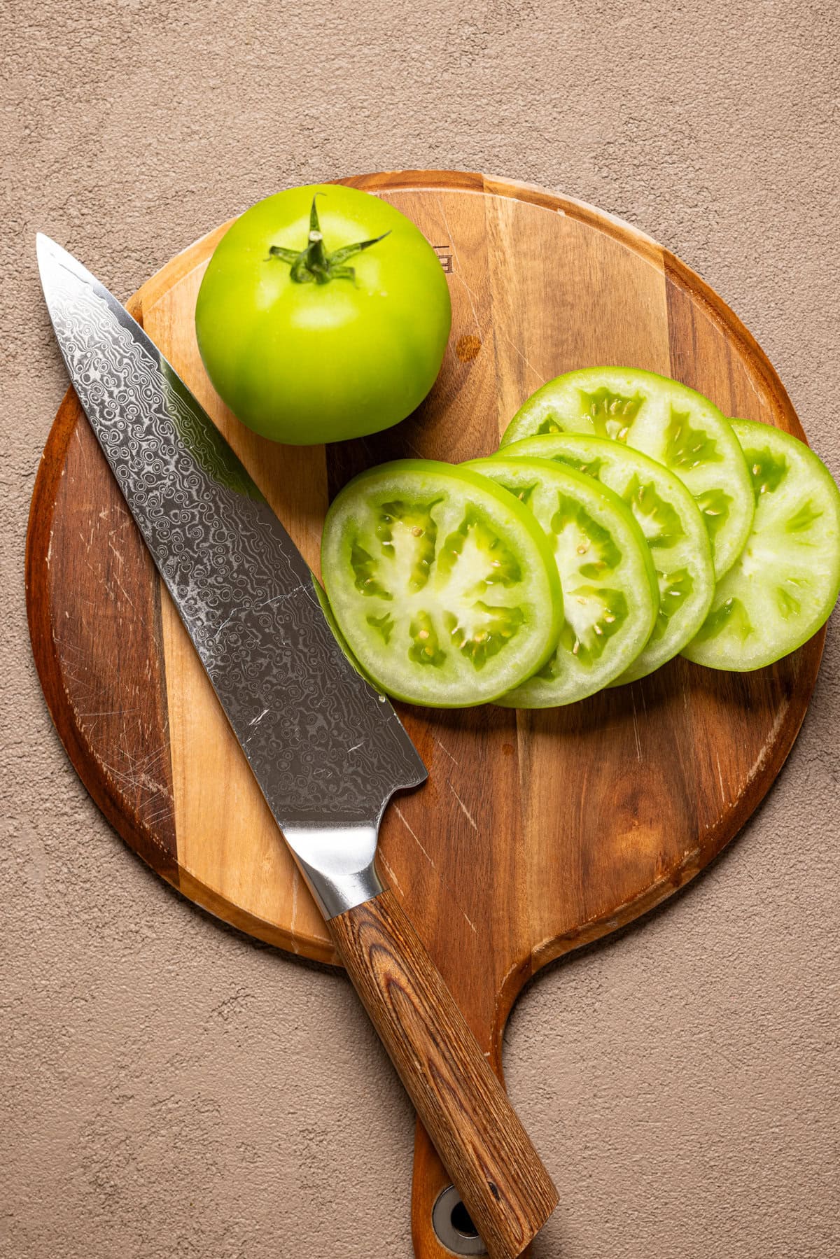 Green tomatoes sliced on a cutting board with a knife.