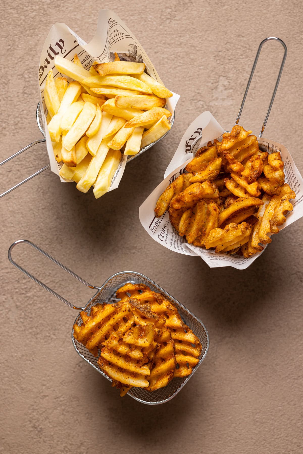 Fries in wire baskets on a brown grey-ish table.