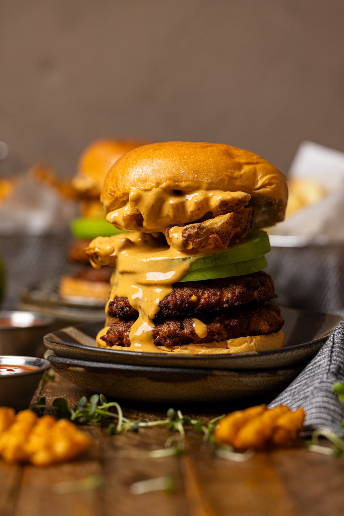 Shot of smash burger on stacked plates with fries in the background.