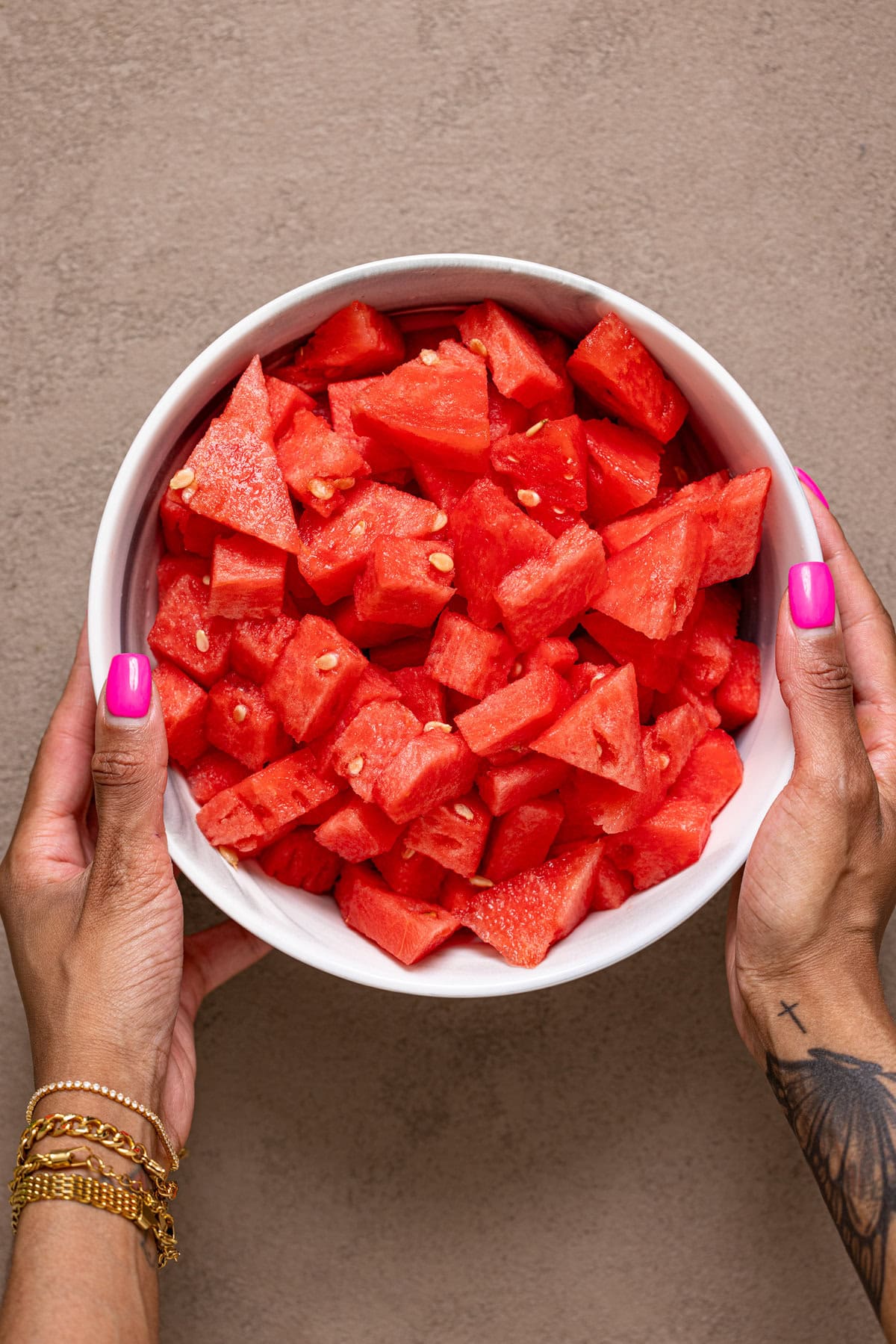 Chopped watermelon in a bowl being held with hands.