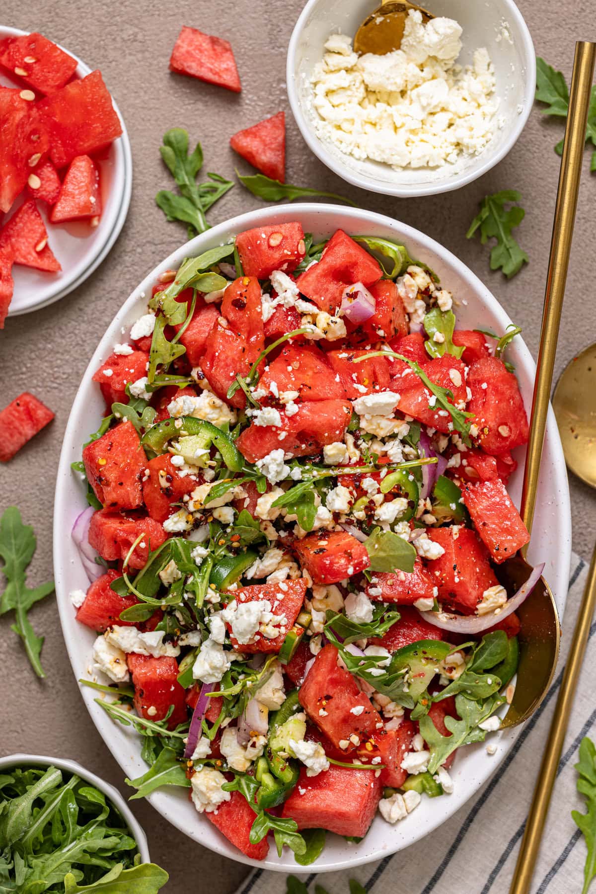 Watermelon salad in a serving dish with with gold spoons.