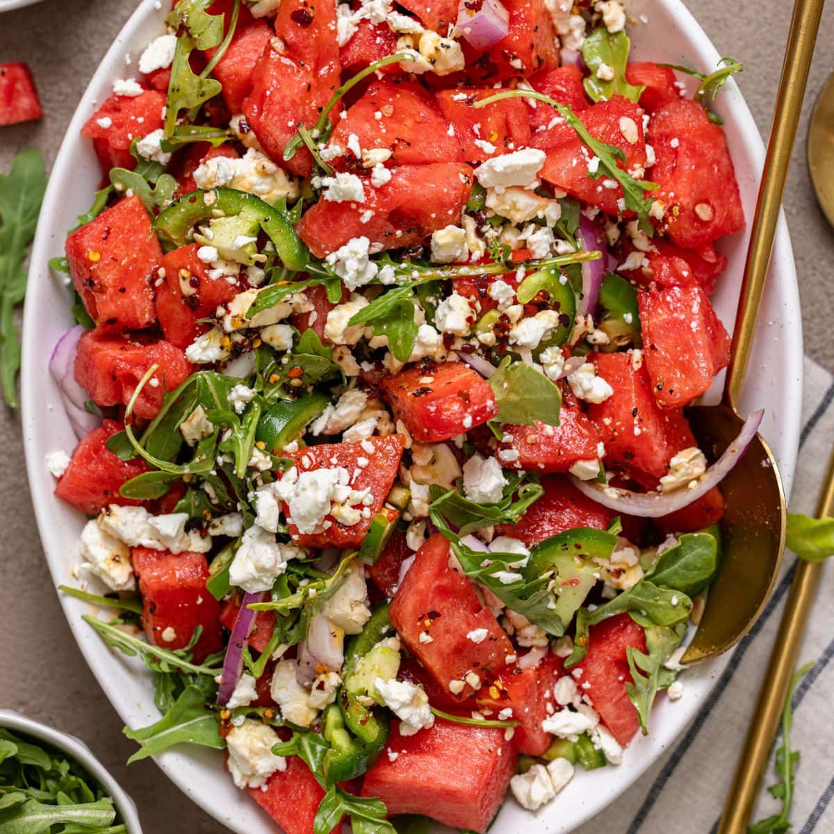 Salad in a white serving dish with gold spoons.