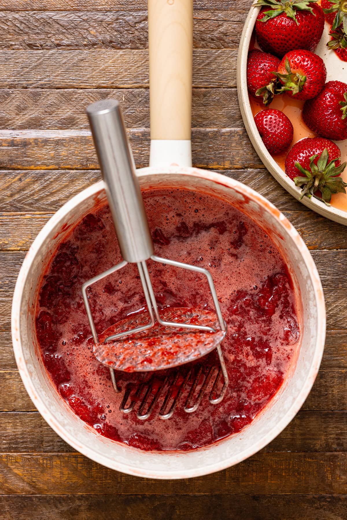 Strawberry jam mixture in a pot with a masher. 