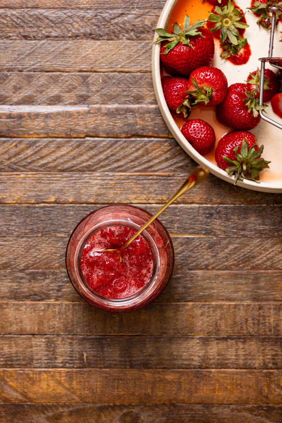 Strawberry jam in a jar with a spoon on brown wood table.