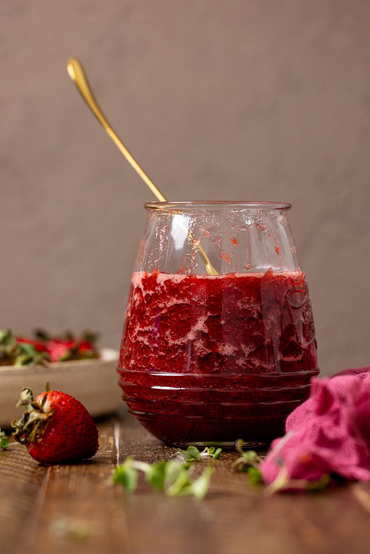 Strawberry jam in a jar with a spoon and strawberries.