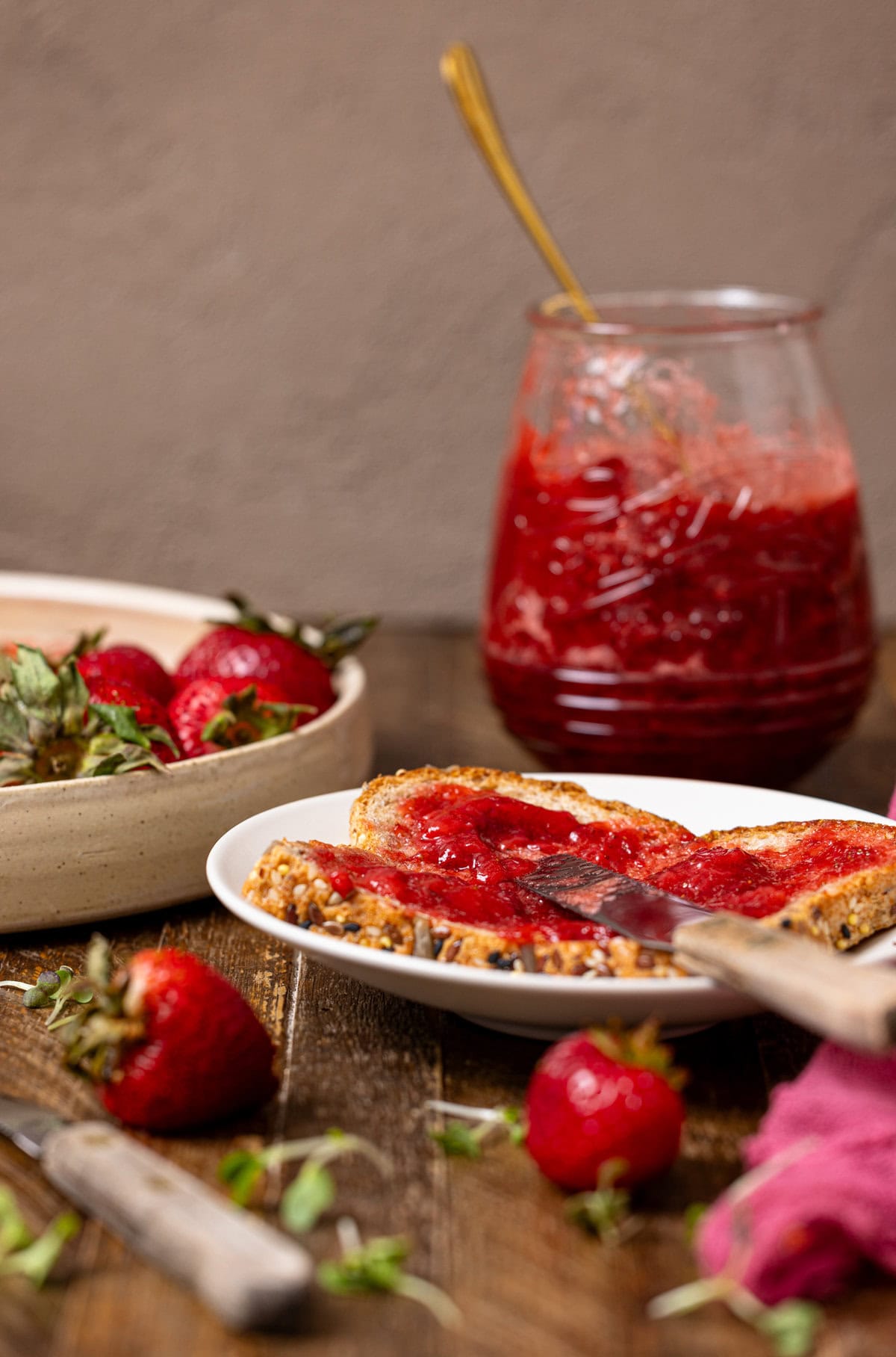 Strawberry jam in a jar with toast on a plate with a knife and strawberries. 