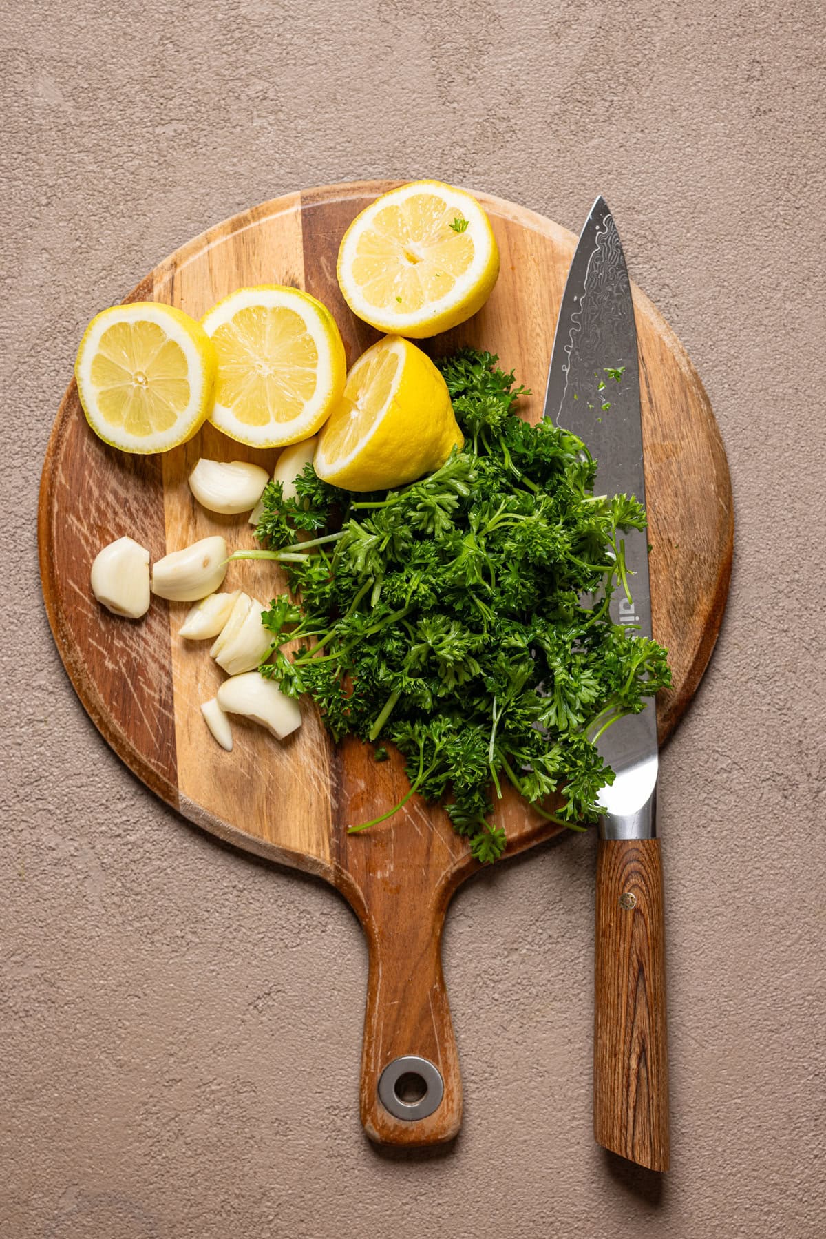 Chopped herbs and lemons on a cutting board with a knife.