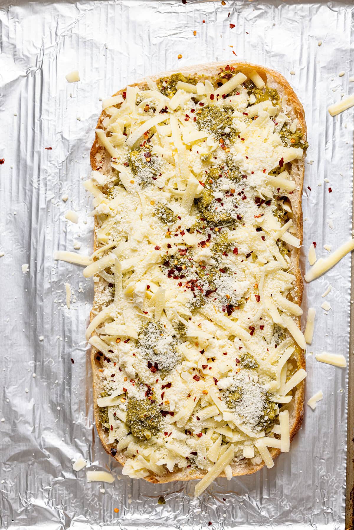 Ingredients layered on sliced rustic bread on a baking sheet with foil paper.