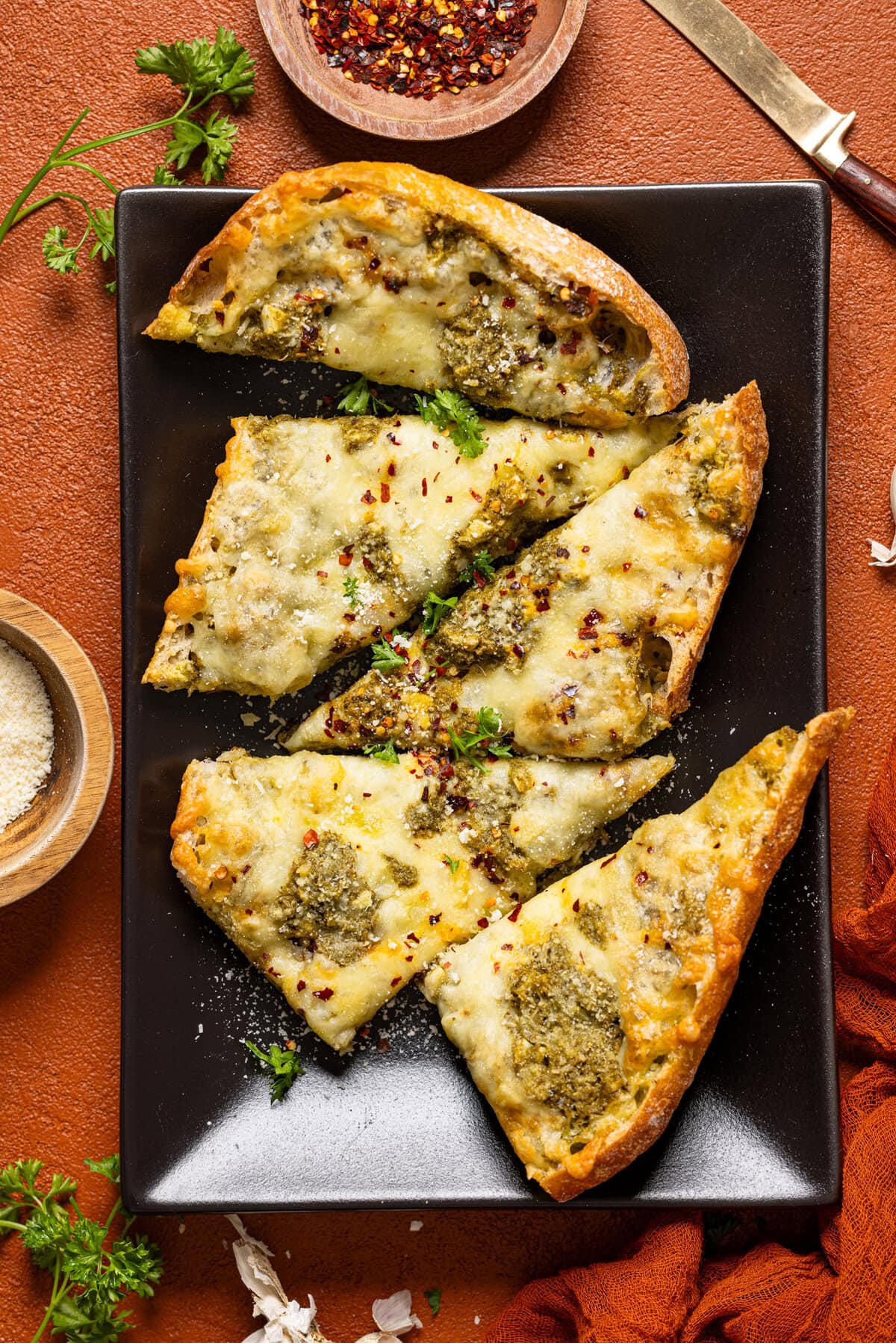 Garlic bread on a black platter with garnish.