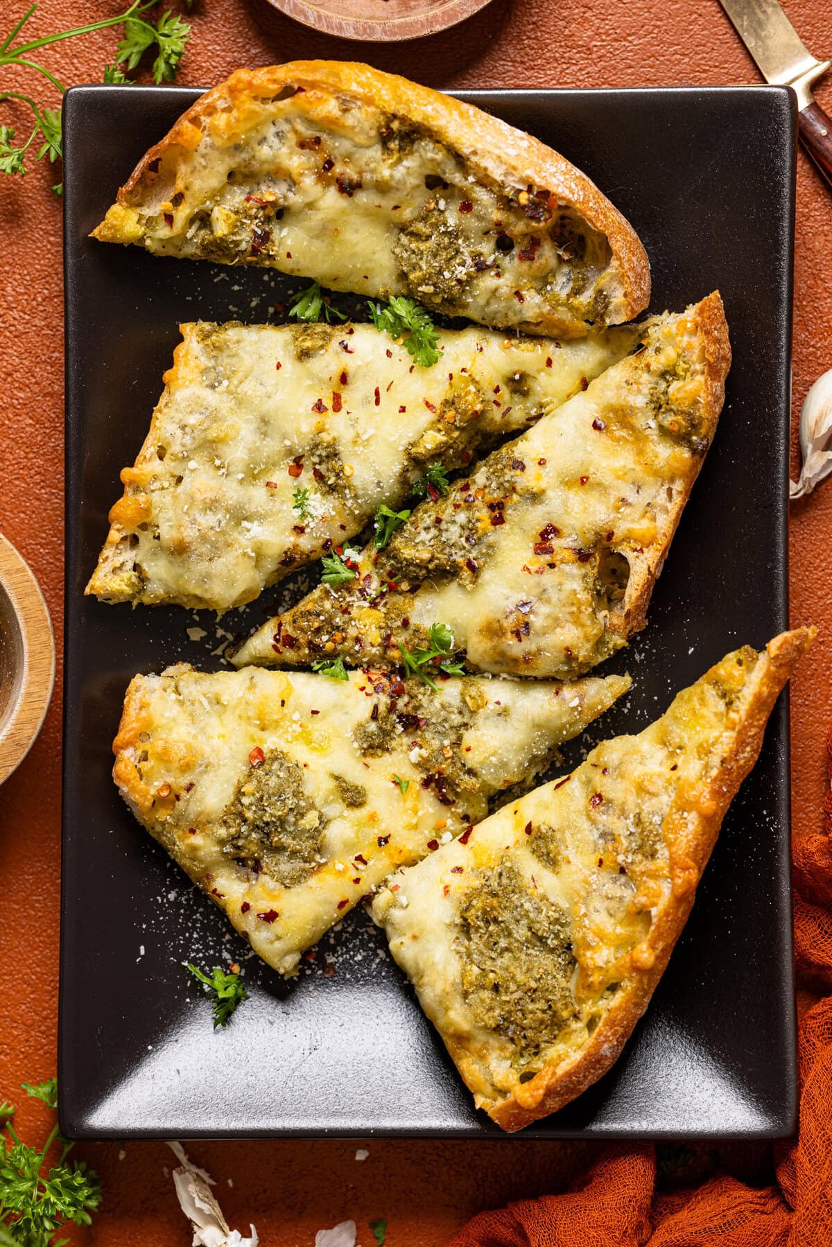 Sliced garlic bread on a black platter with garnish.