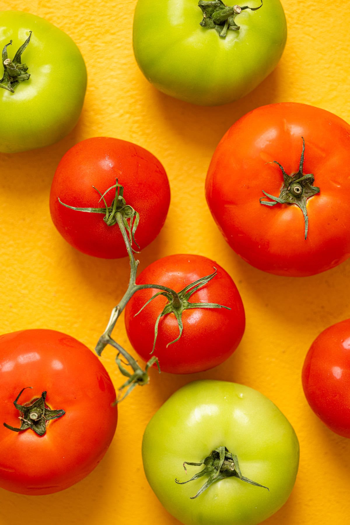 Red and green tomatoes on a yellow table.