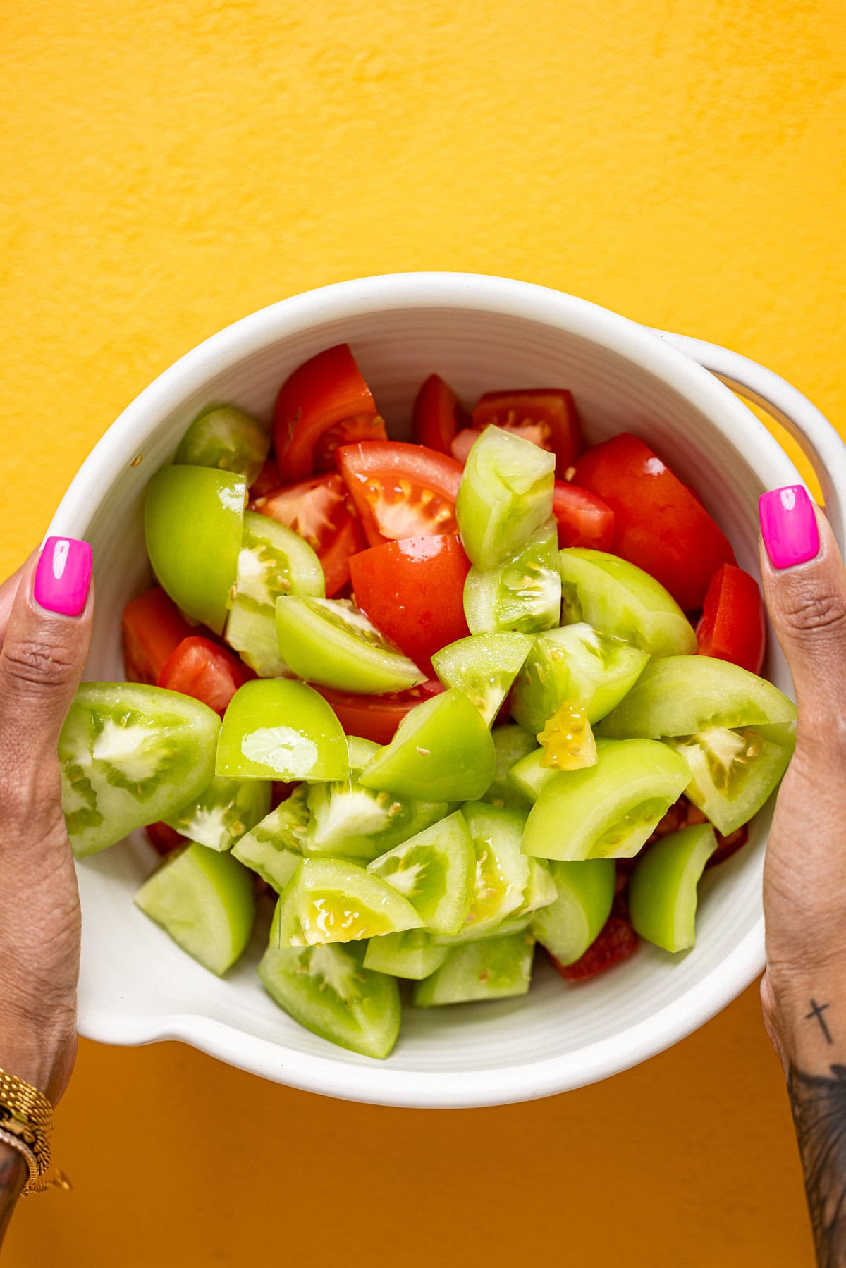 Chopped tomatoes in a white bowl being held by hands.