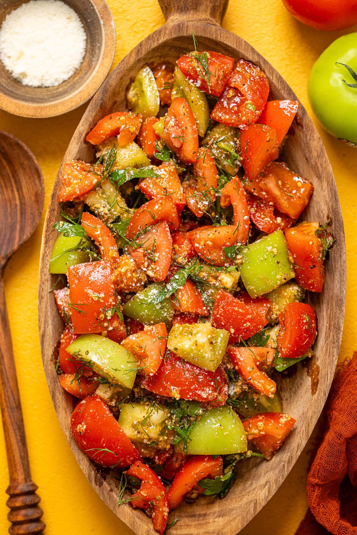 Tomato salad in a wooden serving bowl on a yellow table.