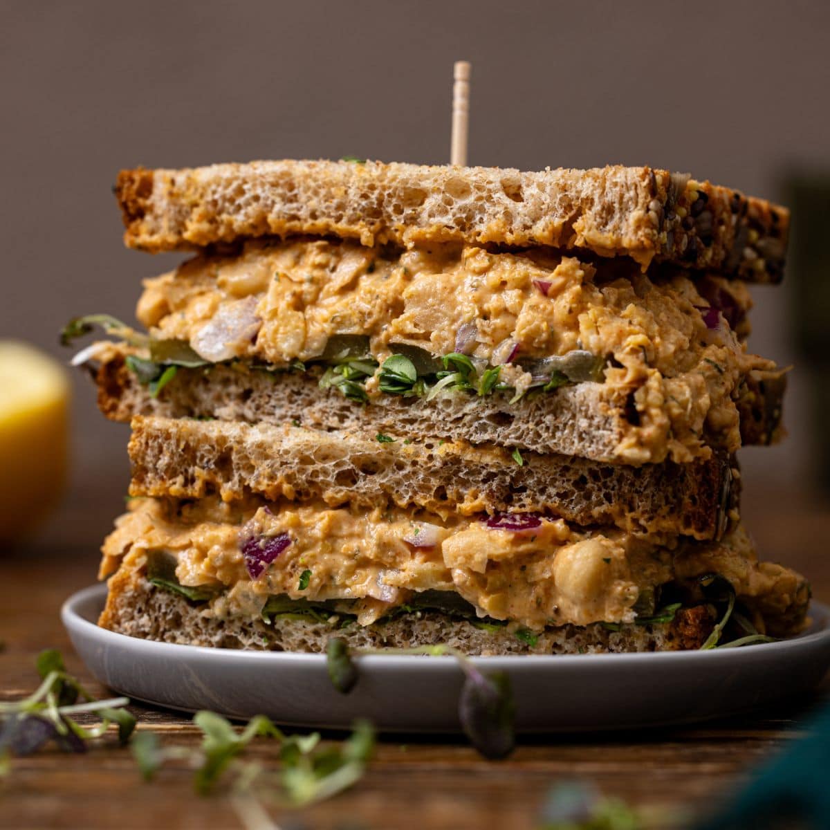 Up close shot of sandwiches stacked on a plate with a toothpick and a lemon.