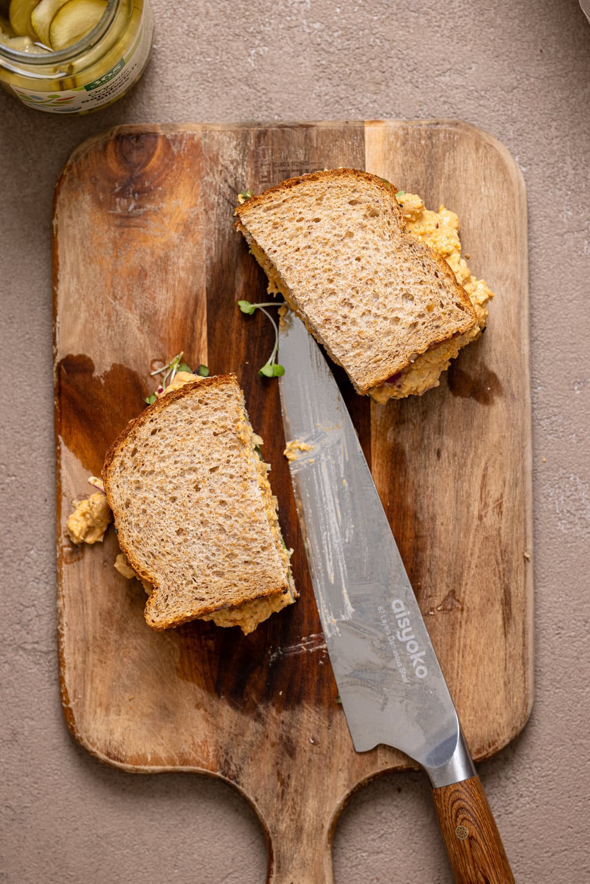 Sandwich cut in half on a cutting board with a knife.